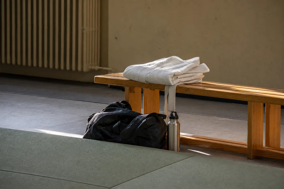 Veste de karategi blanche pliée sur un banc en bois au bord d’un tatami