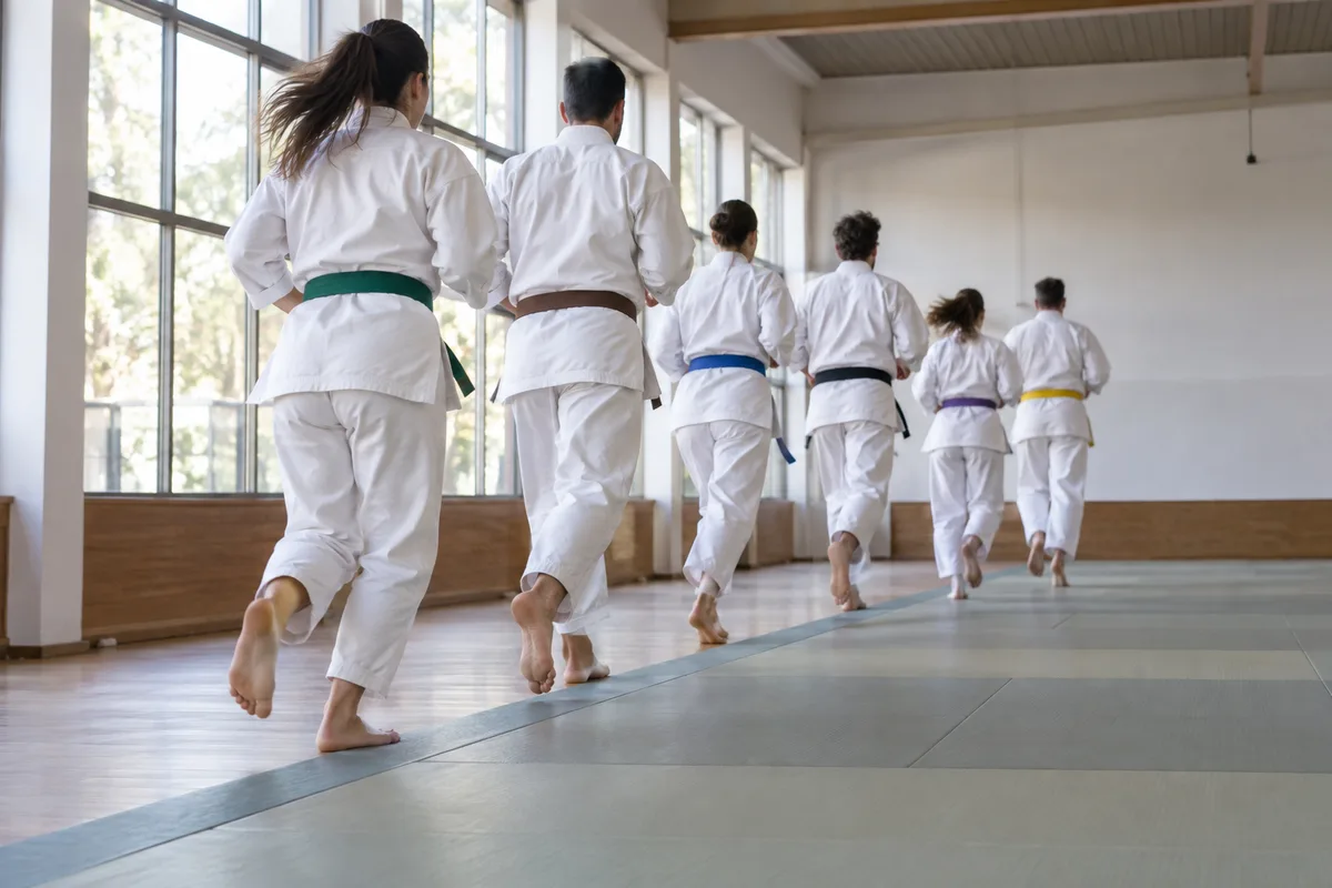 Karatékas en kimono blanc vus de dos courant en ligne sur un tatami pendant l’échauffement