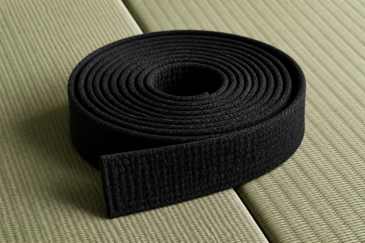 Ceinture noire enroulée posée sur un tatami vert
